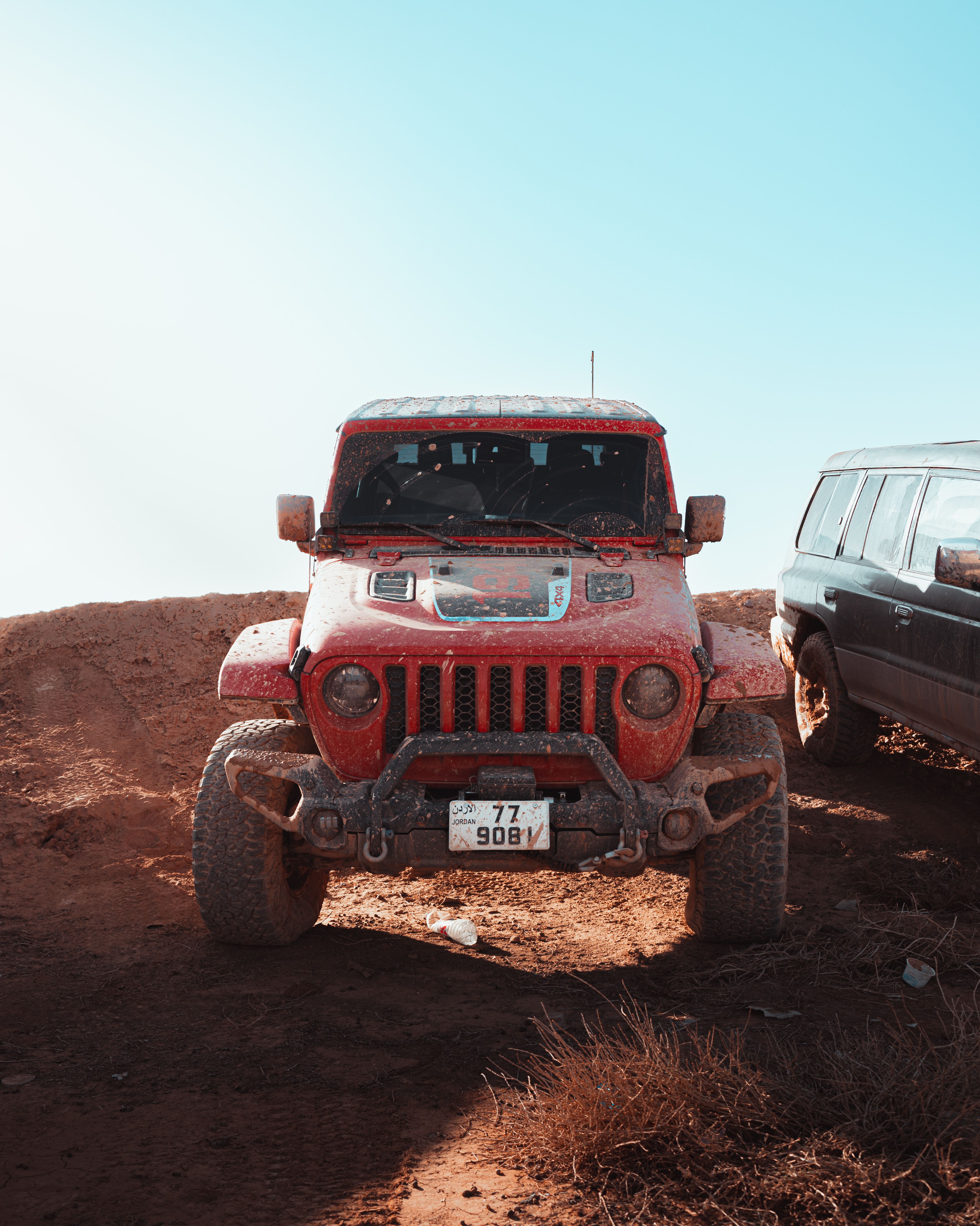 Front view of a red Jeep Wrangler on a dusty off-road trail under a clear blue sky.