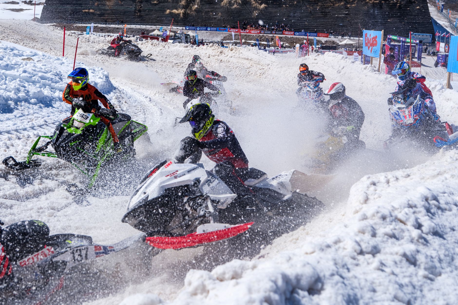 Action-packed snowmobile race on snowy terrain with racers in vibrant gear, capturing speed and excitement.