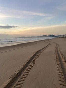 Serene beach scene at sunrise with tire tracks leading to distant mountains.