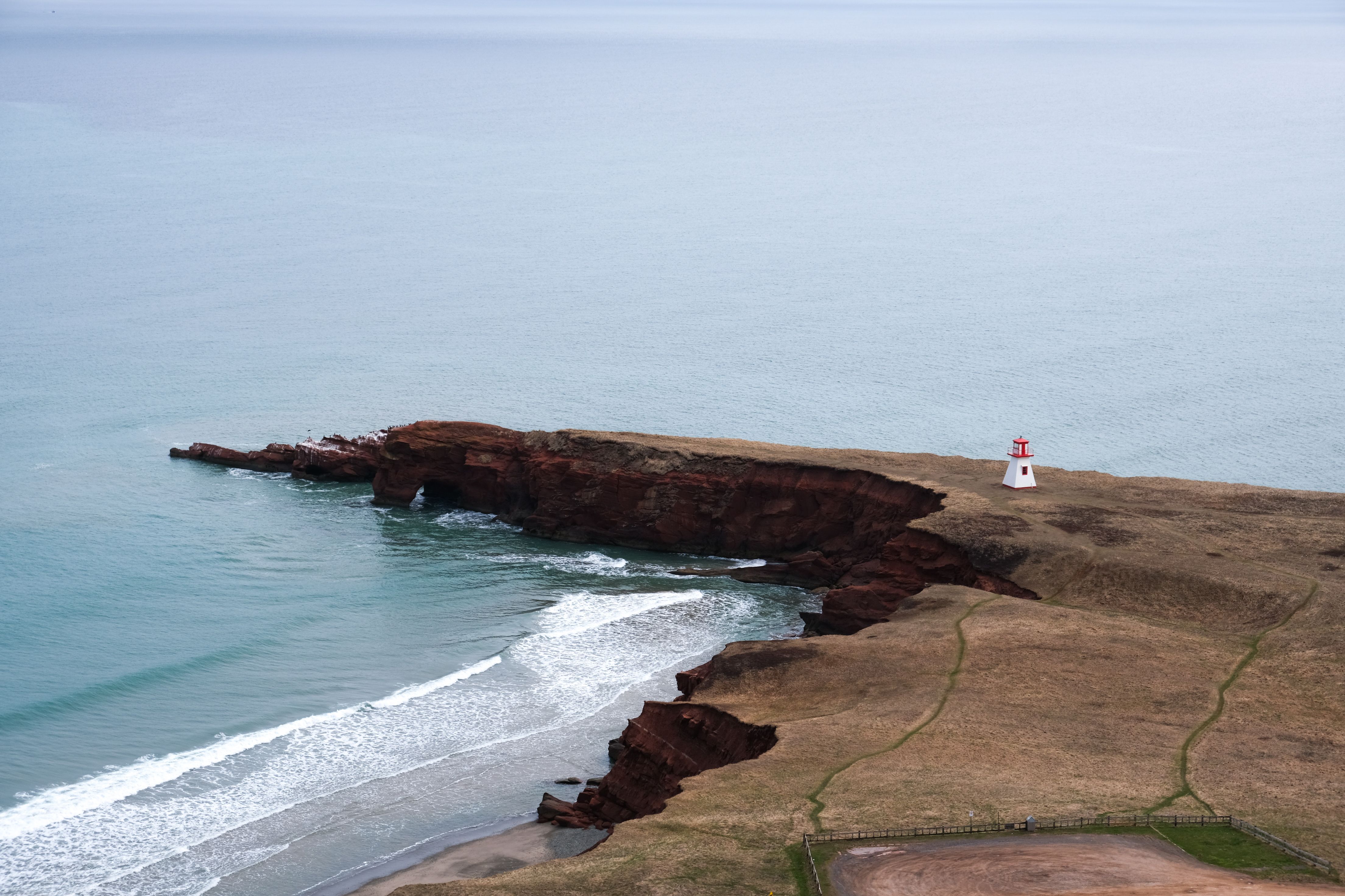 Aerial shot of a coastal cliff and lighthouse against a serene ocean backdrop.