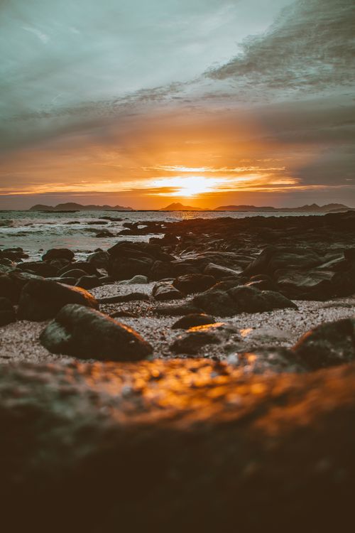 Free Golden sunset over a rocky beach with boulders and waves - serene and breathtaking view. Stock Photo