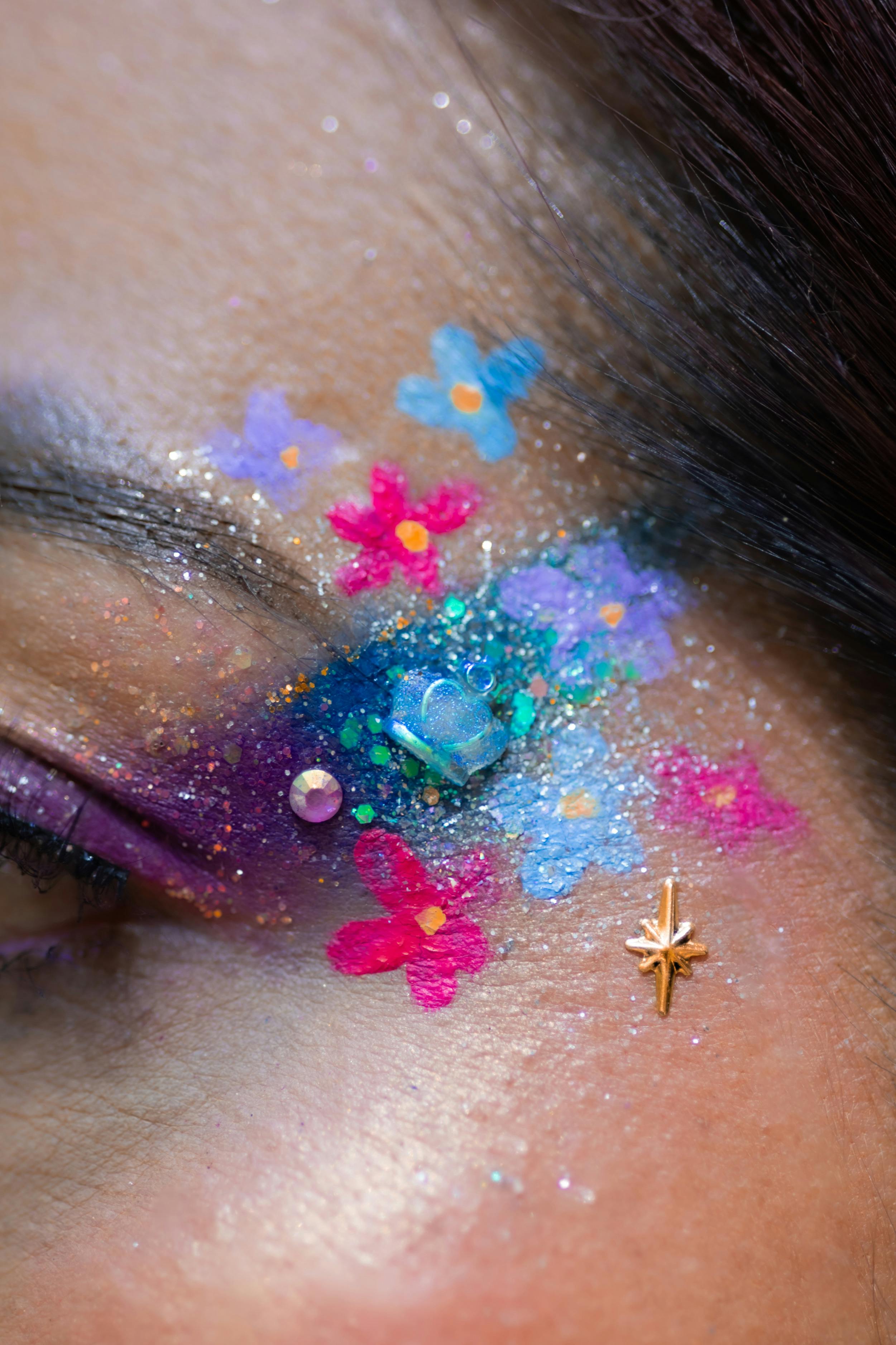 Close-up of vibrant artistic eye makeup with floral and glitter accents.