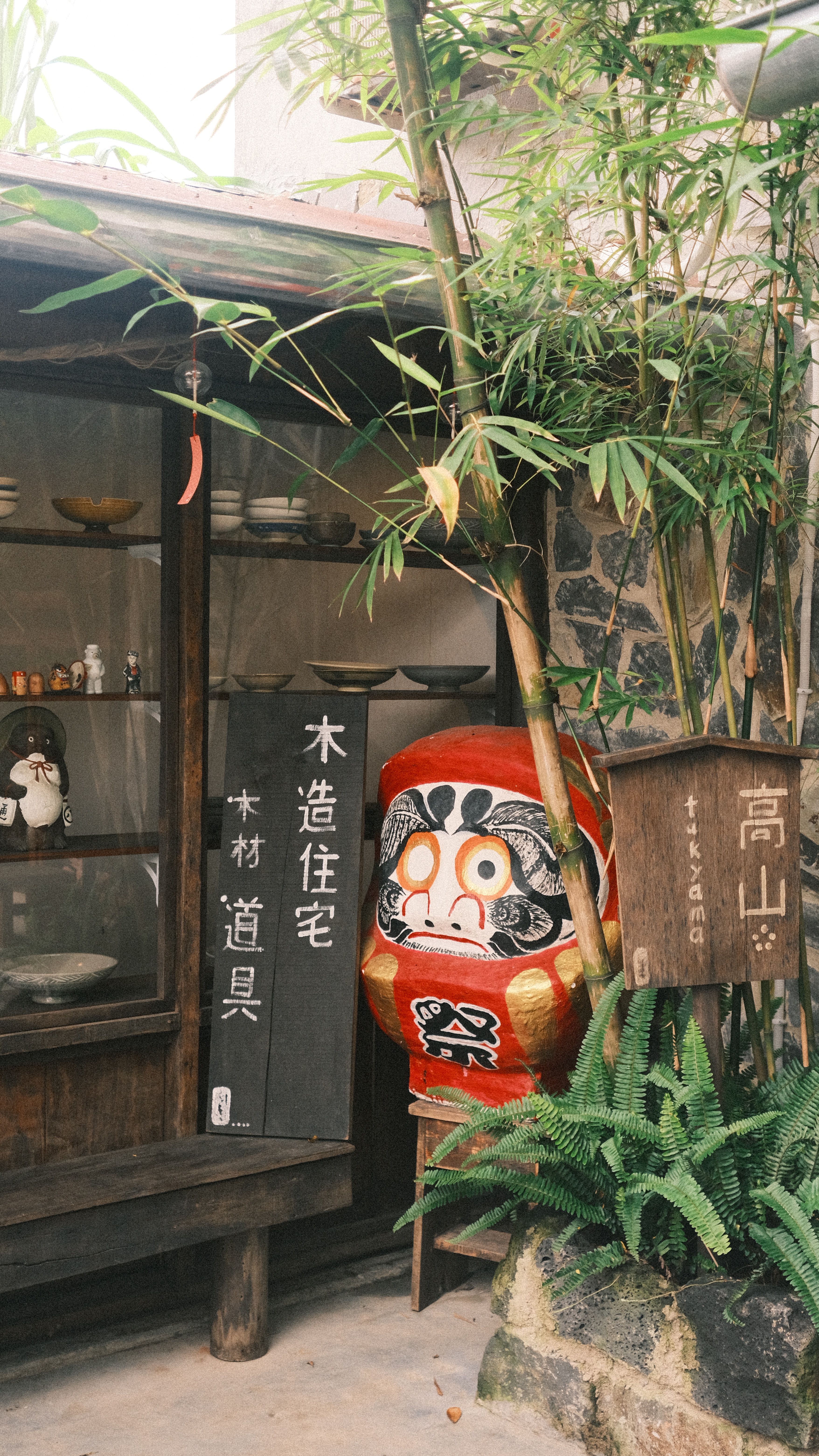 Daruma doll beside wooden structure in serene Japanese garden with bamboo.