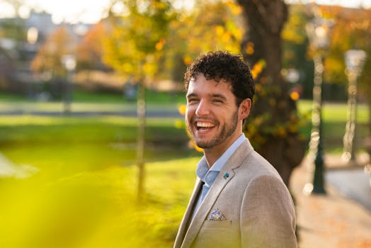 秋天，一位穿着西装的男子在公园里微笑着享受阳光明媚的一天，心情活泼开朗