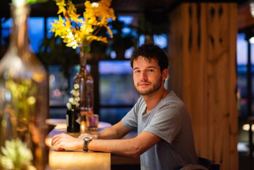 Free Casual man seated at a cozy bar with warm lighting, surrounded by floral decor. Stock Photo