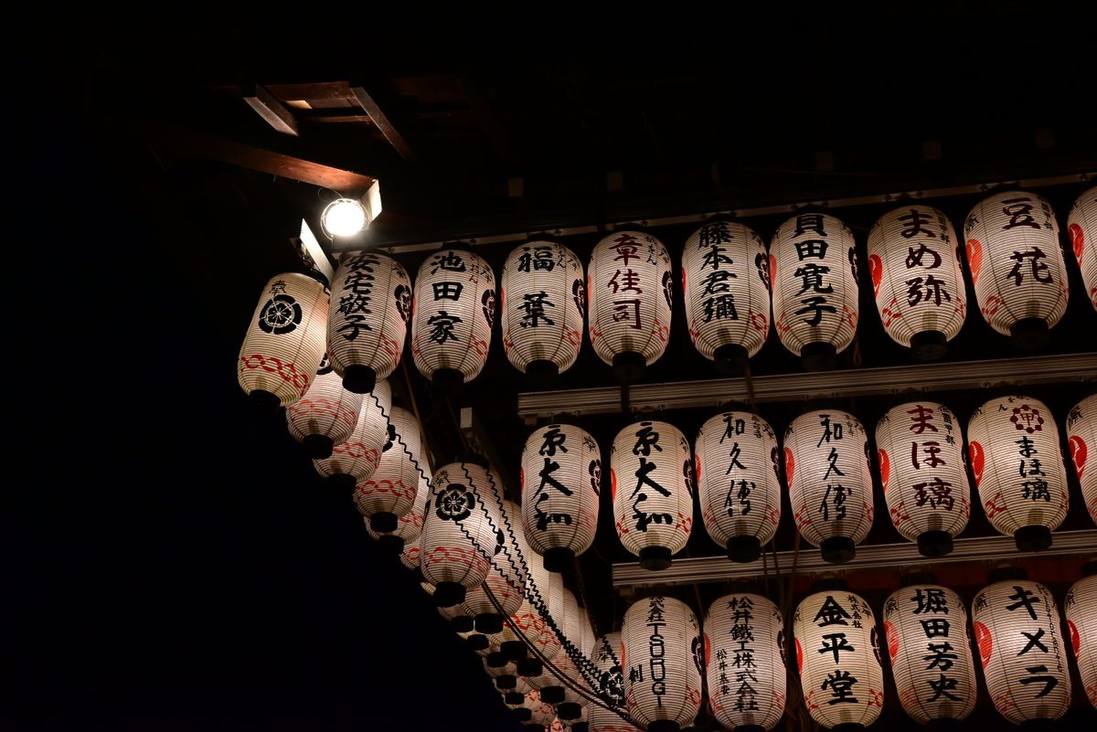 A long row of illuminated traditional Japanese paper lanterns glowing against the dark night during a festival