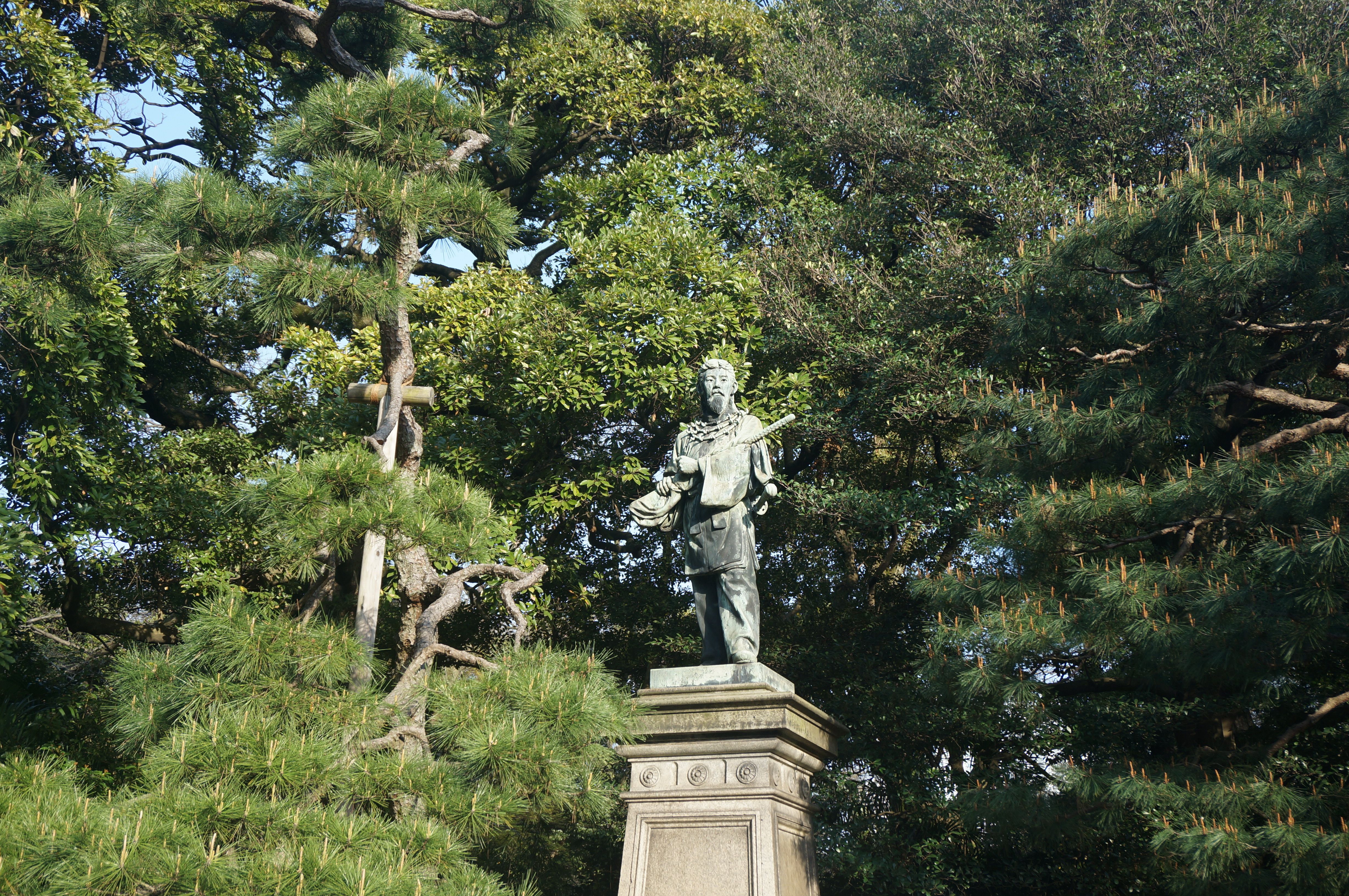 A statue in a park surrounded by lush green trees, captured on a sunny day.