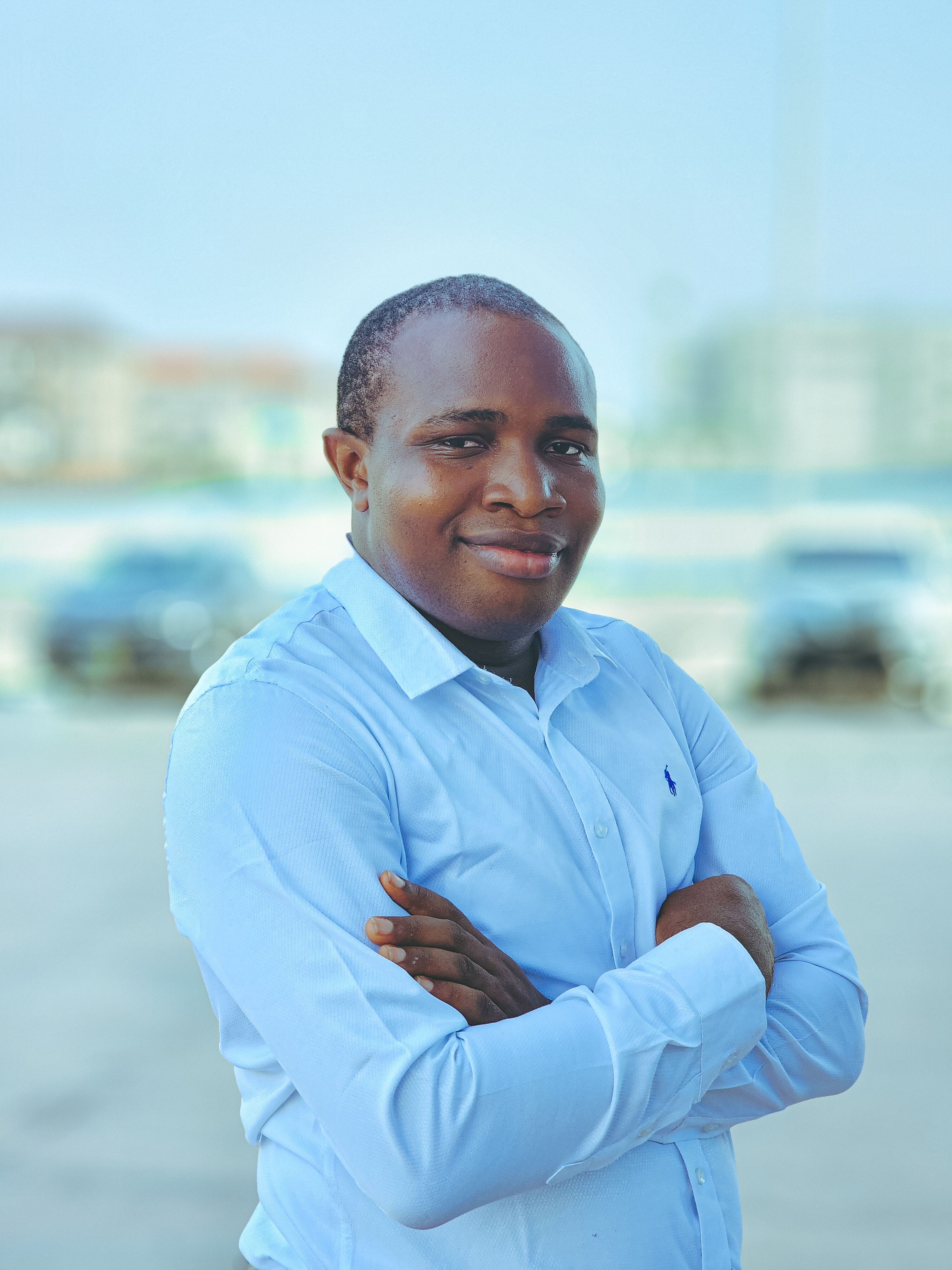 A man standing confidently with arms crossed in an outdoor urban setting.
