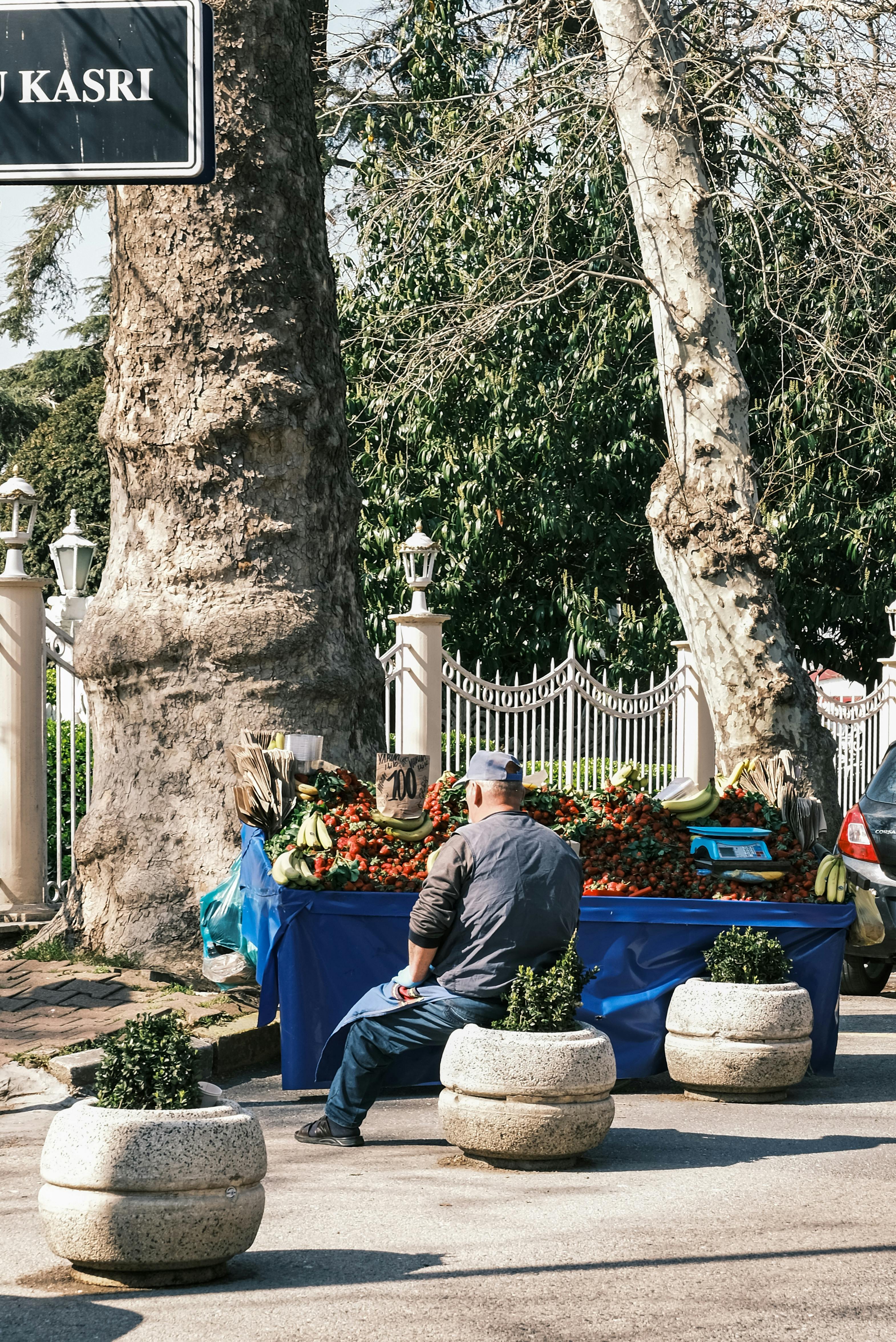 A street vendor sells fresh fruits from a blue-covered stall in a sunny outdoor market.