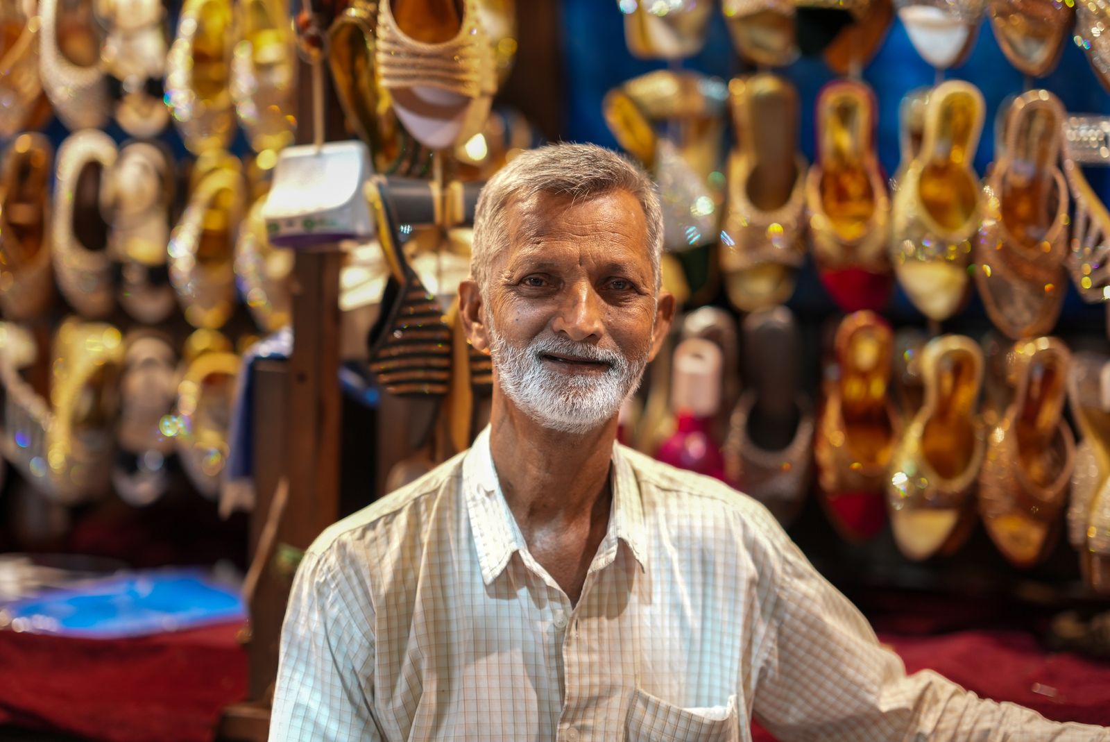 A senior shop owner with a grey beard smiling warmly in his colorful shoe store.