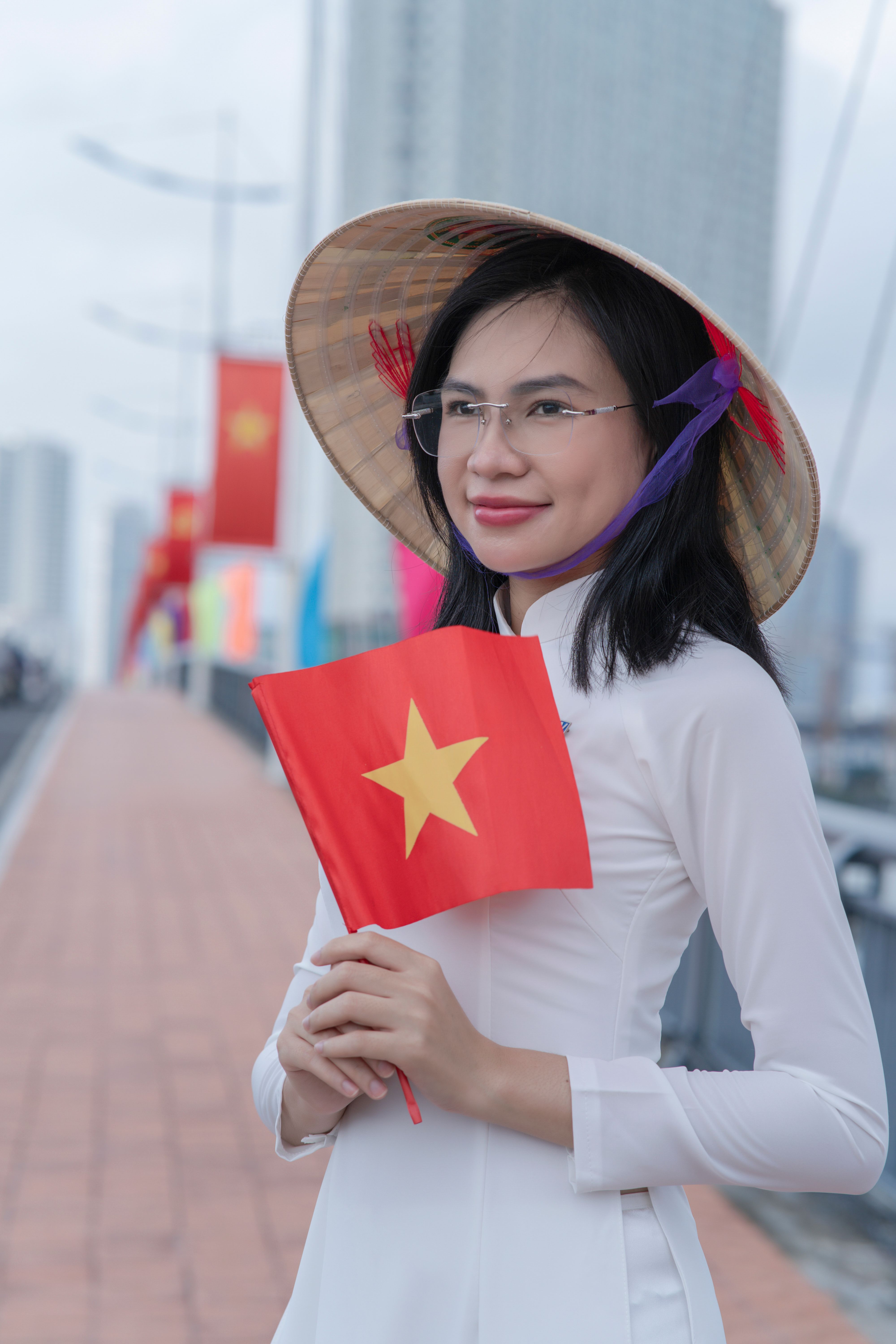 Vietnamese woman in traditional attire holding a flag, standing on a bridge.