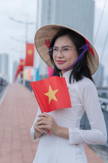 Vietnamese woman in traditional attire holding a flag, standing on a bridge.