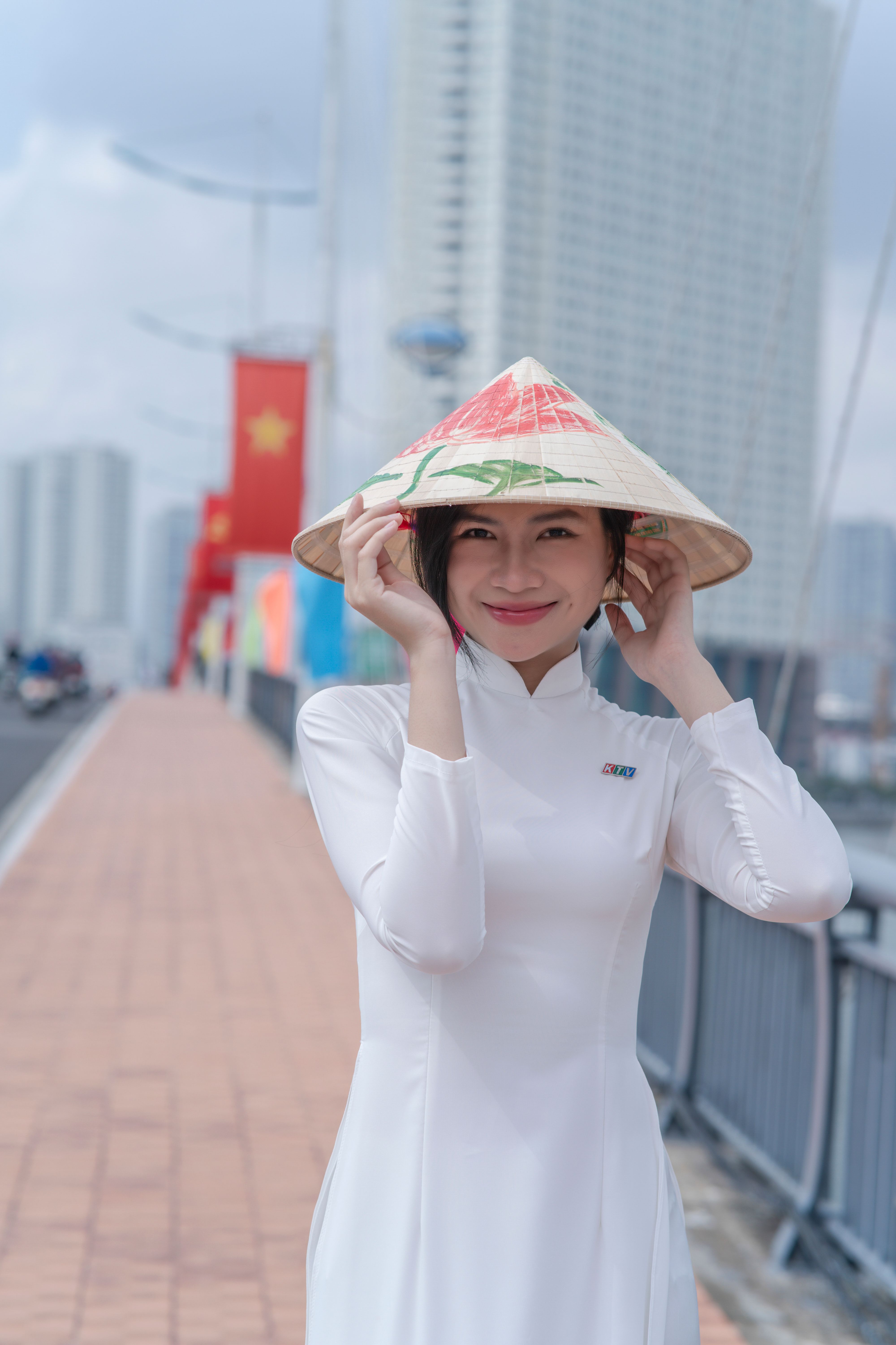 Charming woman wearing a conical hat on a city bridge, showcasing cultural attire.