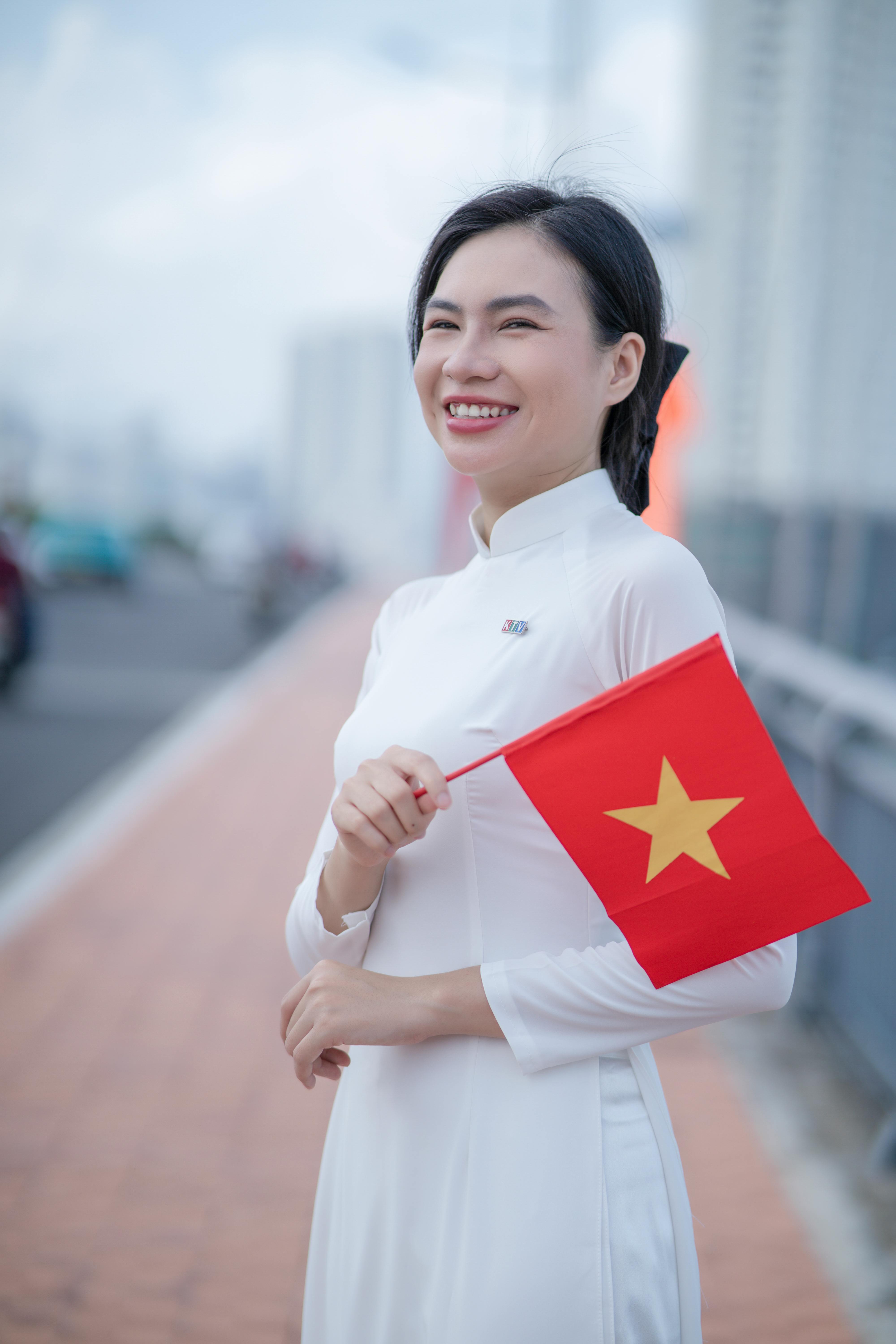 A joyful woman in traditional dress holding a Vietnamese flag on a sunny day.