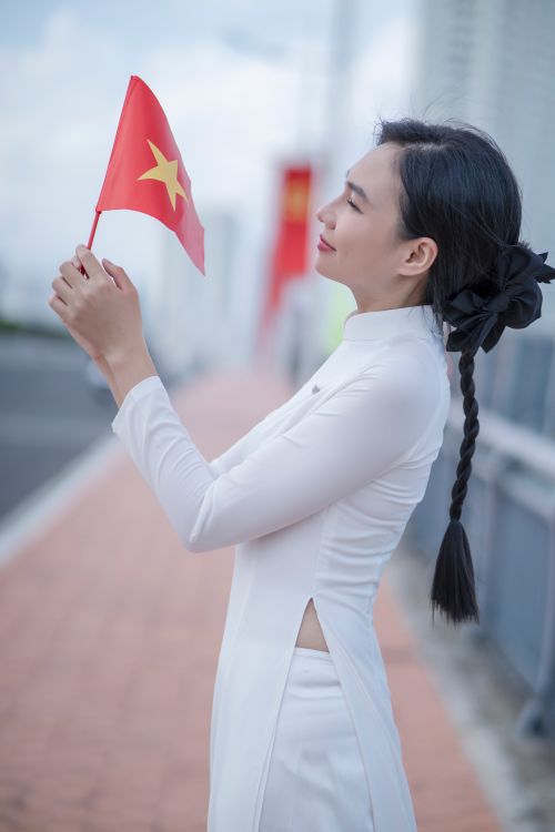 Free A young woman in traditional Vietnamese dress holds a flag, symbolizing patriotism and cultural pride. Stock Photo