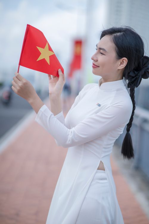 Free Young woman in white áo dài holding Vietnam flag on a sunny day. Stock Photo