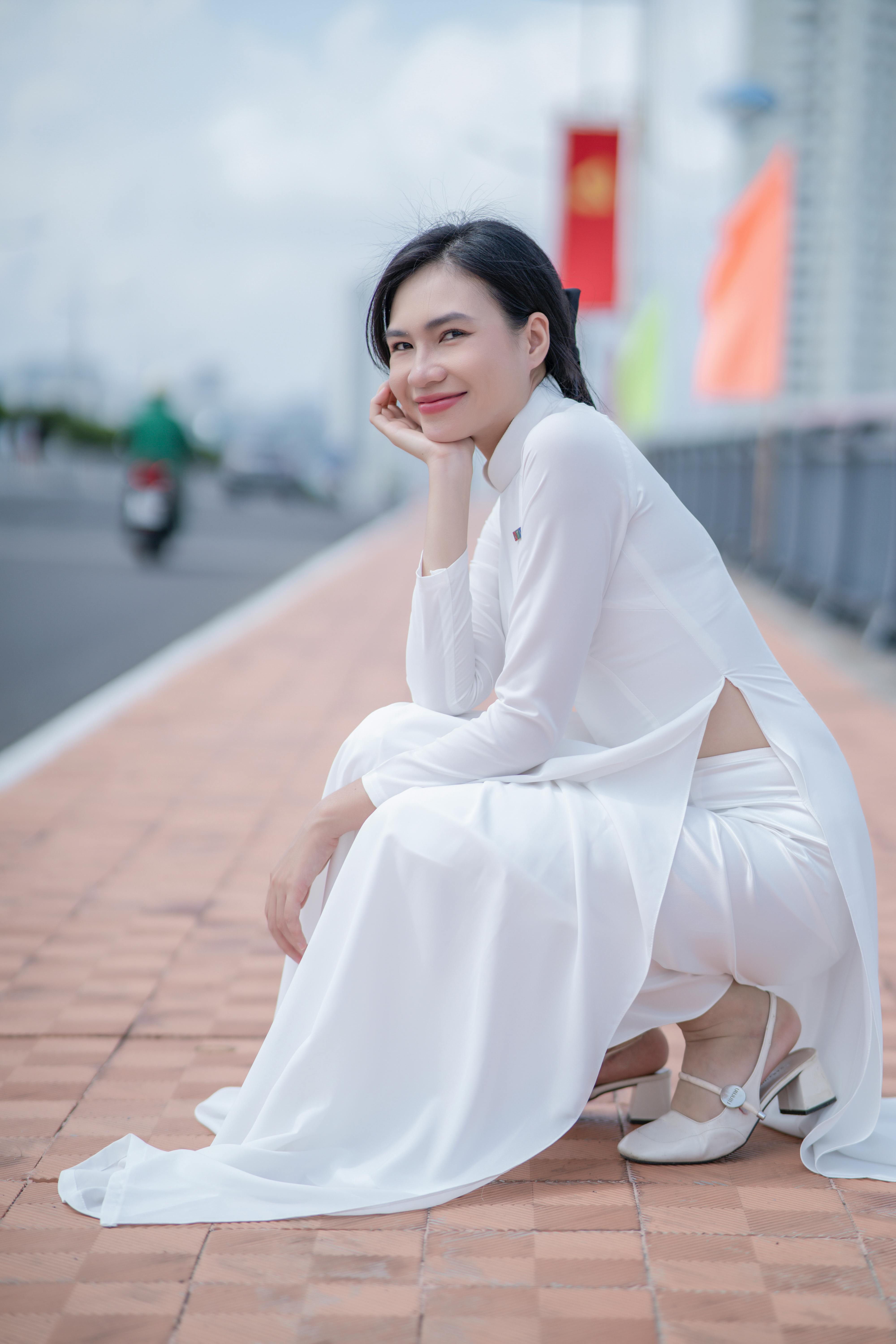 Stylish woman in white dress poses gracefully outdoors on a sunny day.