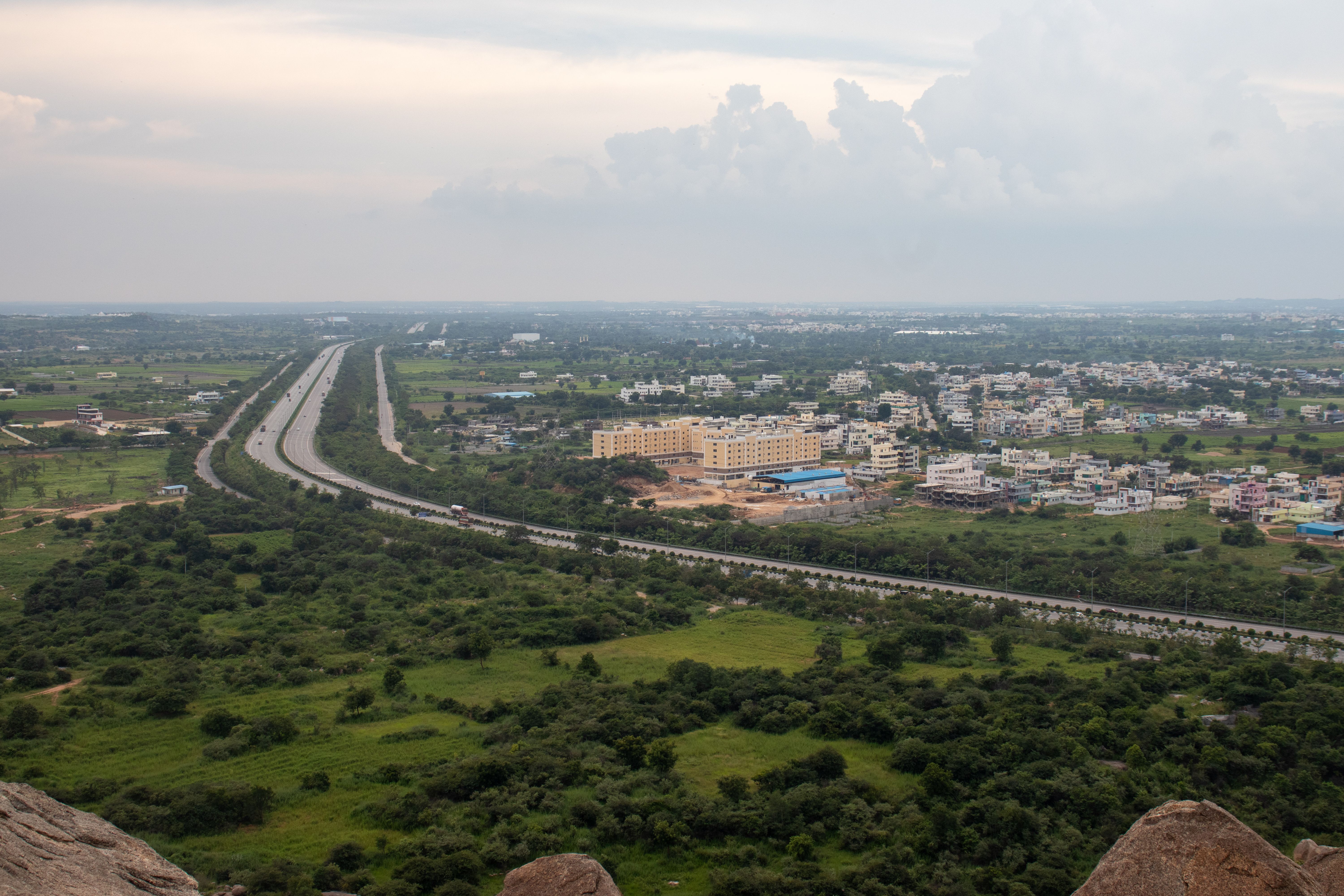 Aerial view of a lush green Indian landscape with a highway stretching through fields and residential areas. | Indian Village Development