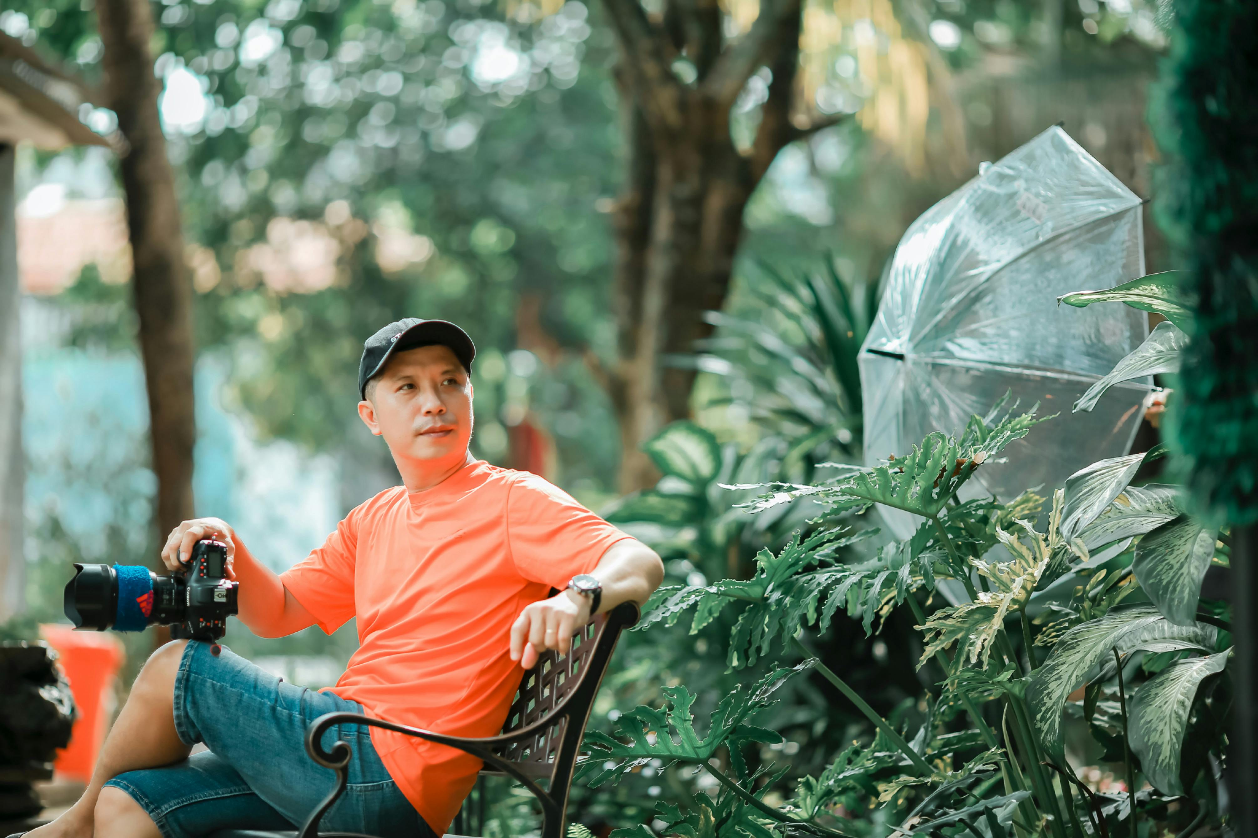 Photographer seated in a vibrant outdoor garden setting holding a camera.