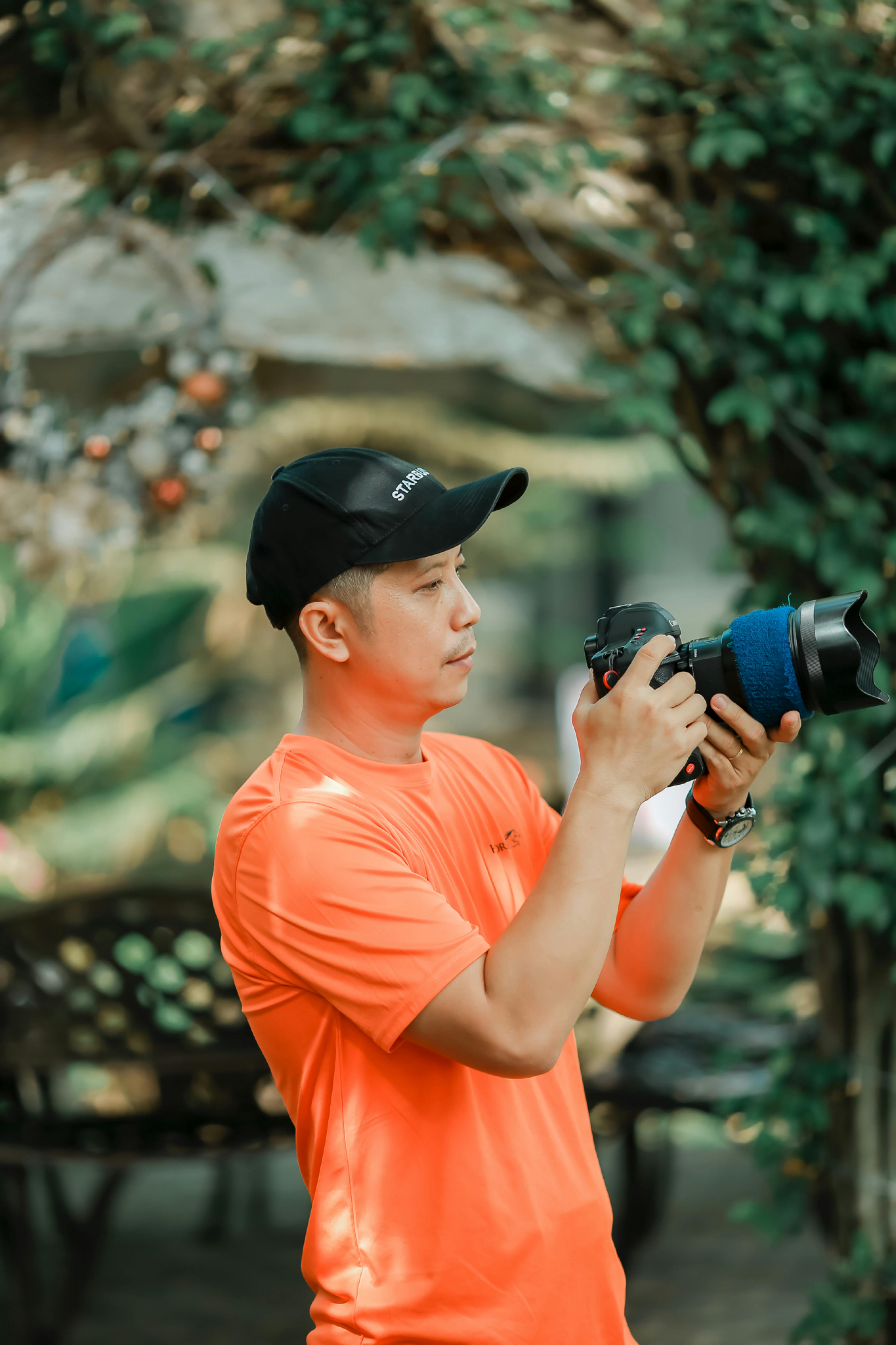 Photographer in bright orange shirt taking pictures outdoors, showcasing equipment handling skill.