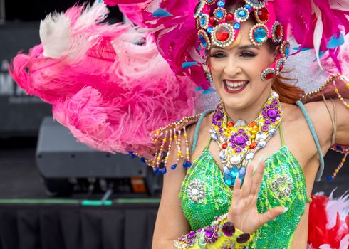 Joyful carnival performer in vibrant costume with feathered headdress, smiling and dancing.