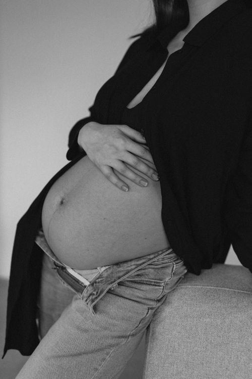 Free A stylish black and white maternity portrait capturing a pregnant woman's baby bump indoors. Stock Photo