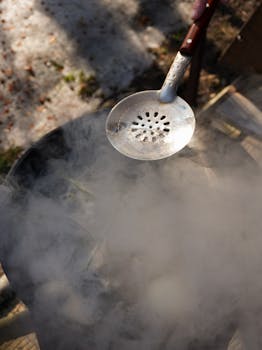 An overhead view of a steaming pot outdoors with a slotted spoon.