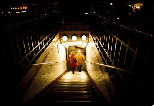 A couple descends a dimly lit subway entrance at night, creating a moody urban scene.