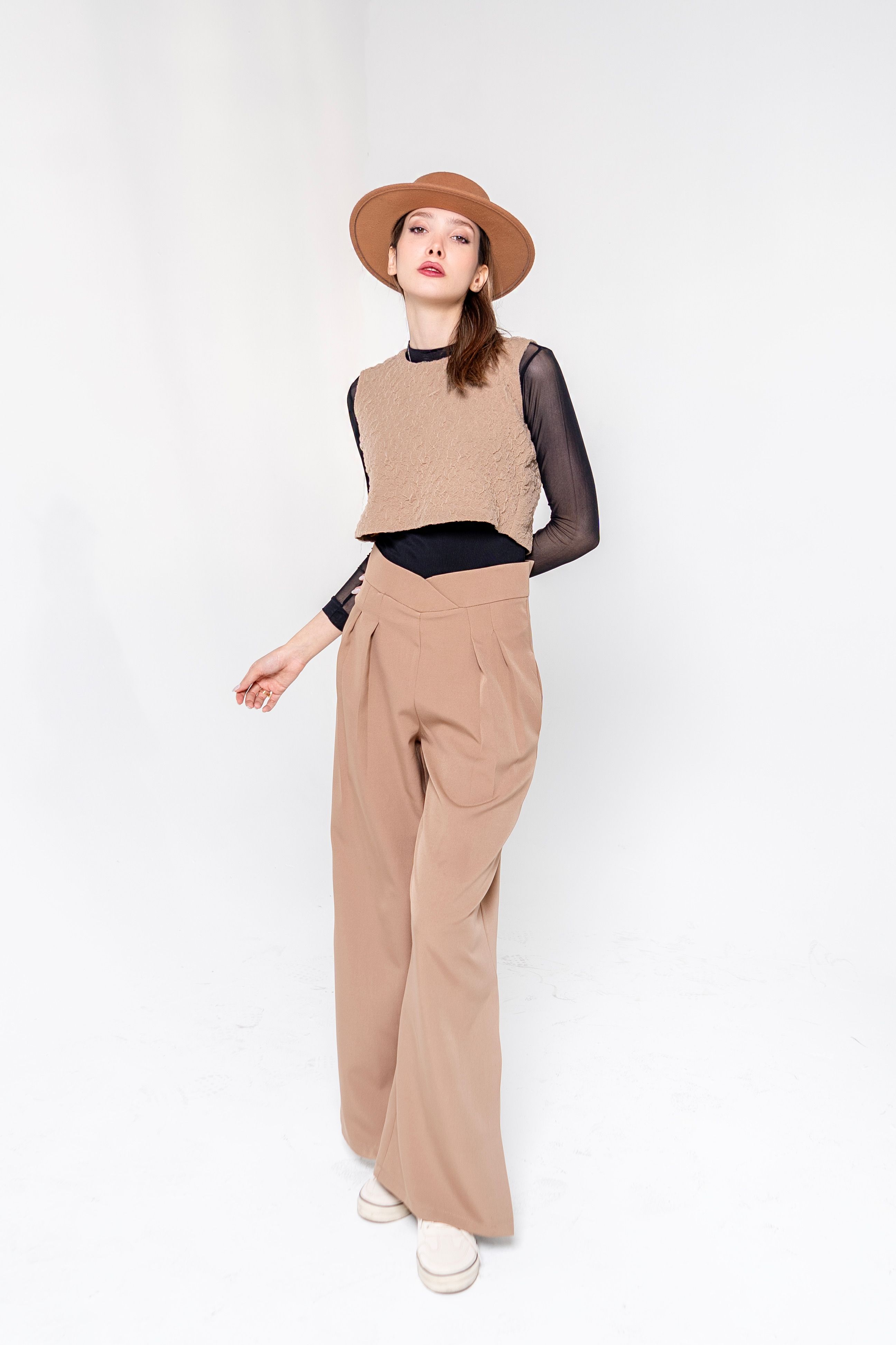 Fashionable woman wearing beige sweater and wide-leg pants in studio.