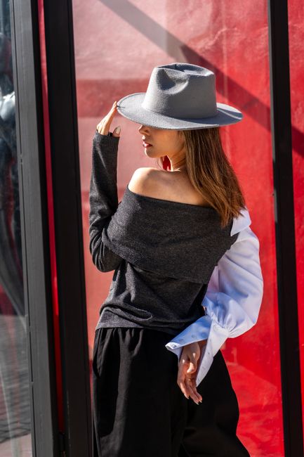 Fashionable woman in stylish hat poses against a bold red backdrop.