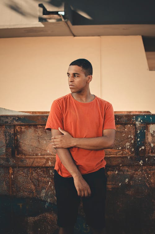 Photo of Man in Orange T-shirt and Black Shorts Posing While Looking Away