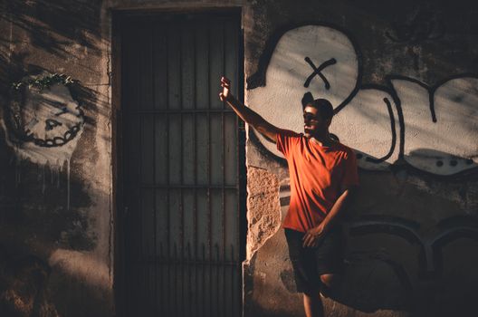 A man in casual wear leaning against a graffiti-covered wall, casting a dramatic shadow.
