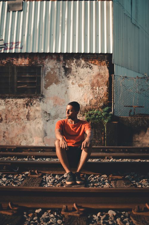 Free A young man in casual attire sits on railway tracks, set against an urban backdrop. Stock Photo