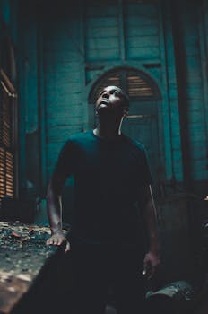 一名男子站在一栋光线昏暗的废弃建筑里，戏剧性地抬头，脸上带着表情