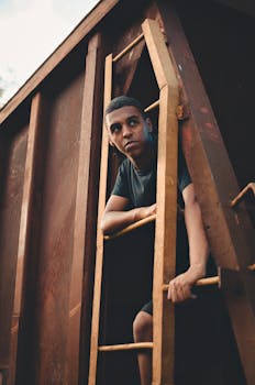 一名年轻的黑人男子在工业环境的梯子上摆姿势，展现时尚与风格