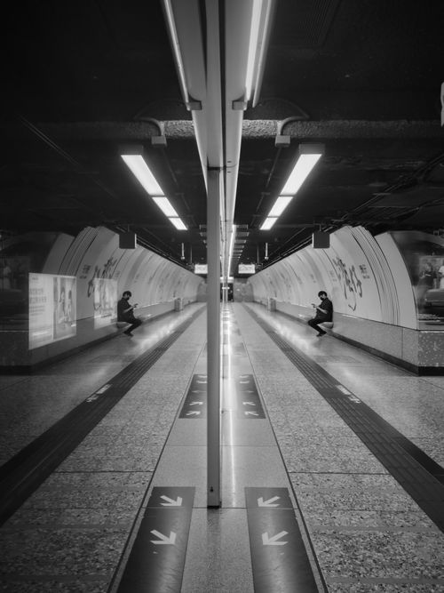 Free A black and white photo capturing symmetry in a Hong Kong subway station with commuters. Stock Photo