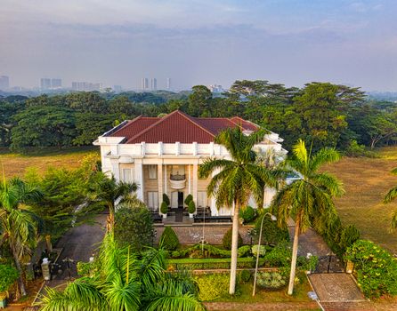 Aerial shot of a grand mansion with red roof and palm trees in the scenic landscape of Banten, Indonesia.