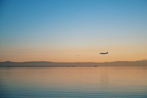 Free A serene scene of an airplane flying over calm ocean waters during sunset. Stock Photo