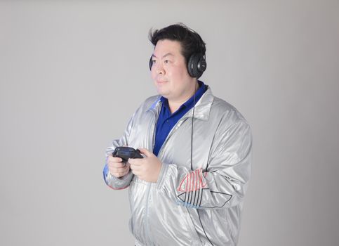 A man wearing headphones and a silver jacket holding a game controller, enjoying his gaming session.
