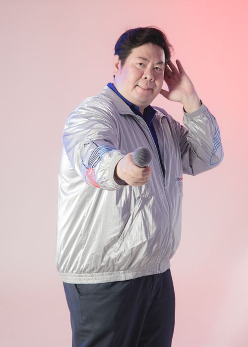 Free Adult male in a silver jacket holding a microphone, posing confidently against a colorful backdrop. Stock Photo