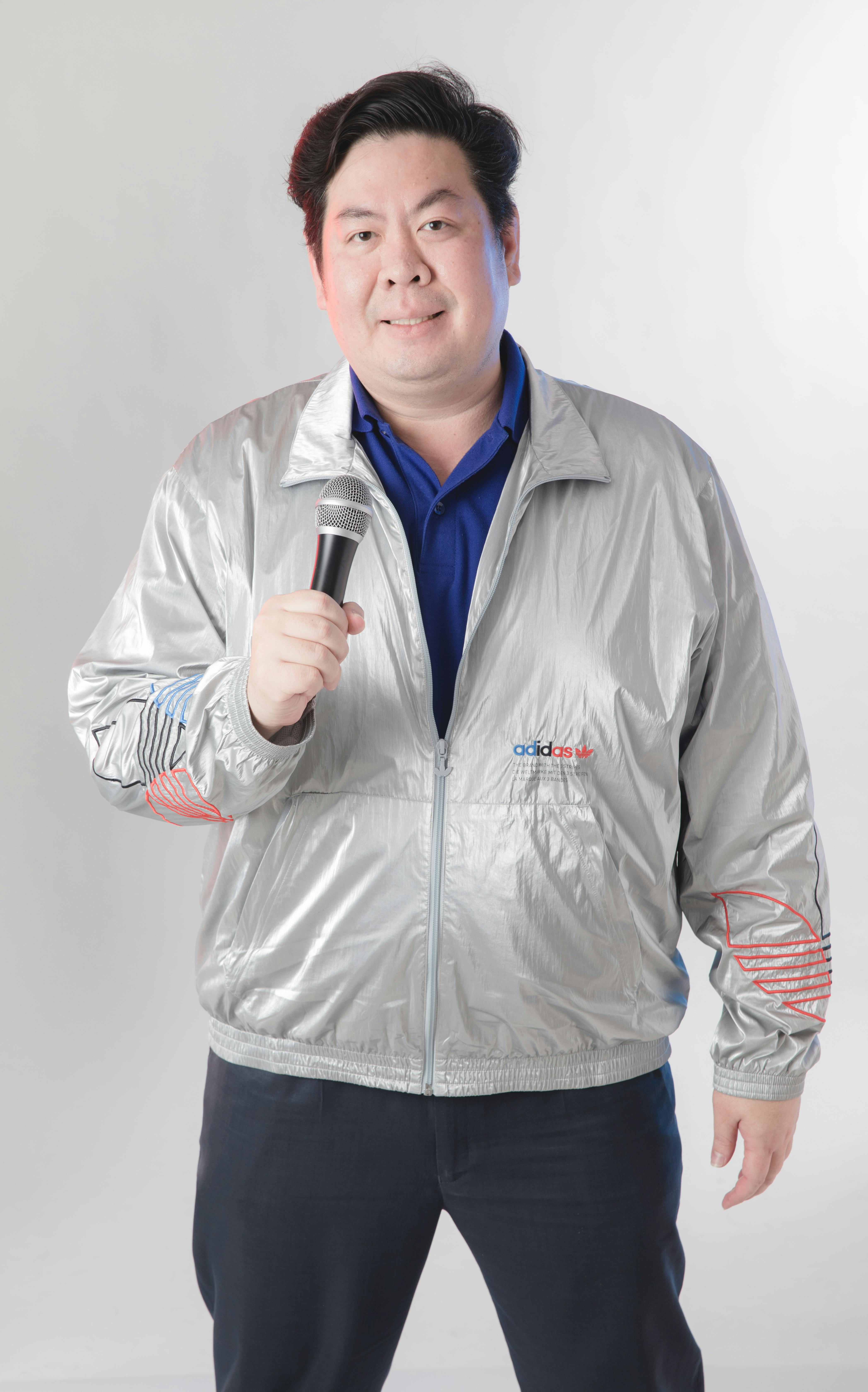 무료 중립적인 배경에서 자신 있게 마이크를 잡고 있는 은색 재킷을 입은 남자. 스톡 사진