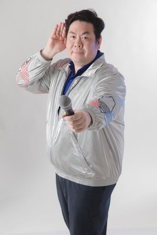 Free Asian male performer with microphone in a silver jacket posing energetically, ideal for entertainment themes. Stock Photo