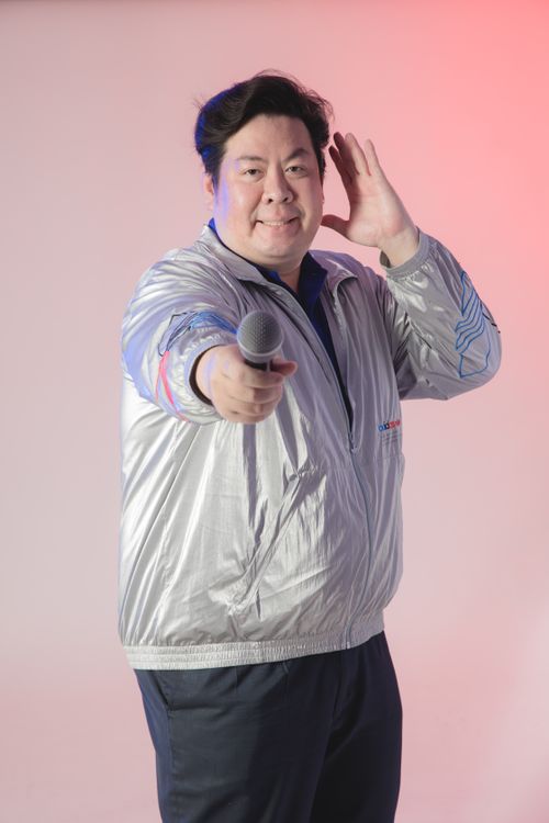 Free Smiling man in silver jacket holding microphone, performing on stage. Stock Photo