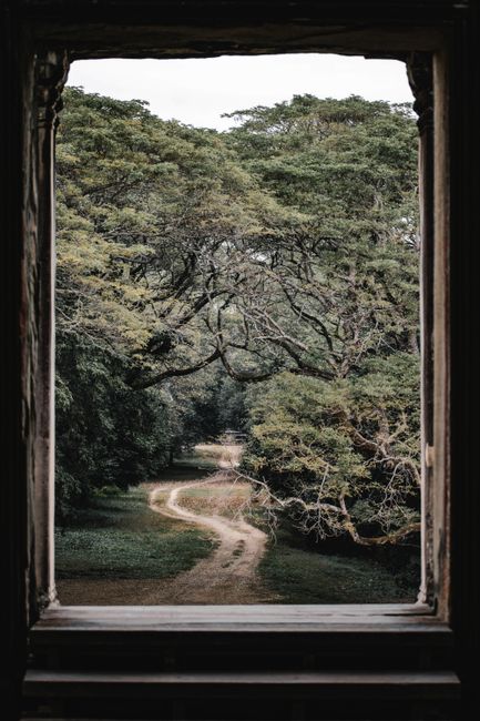 Serene view of a winding forest path framed by an ancient window in Cambodia.