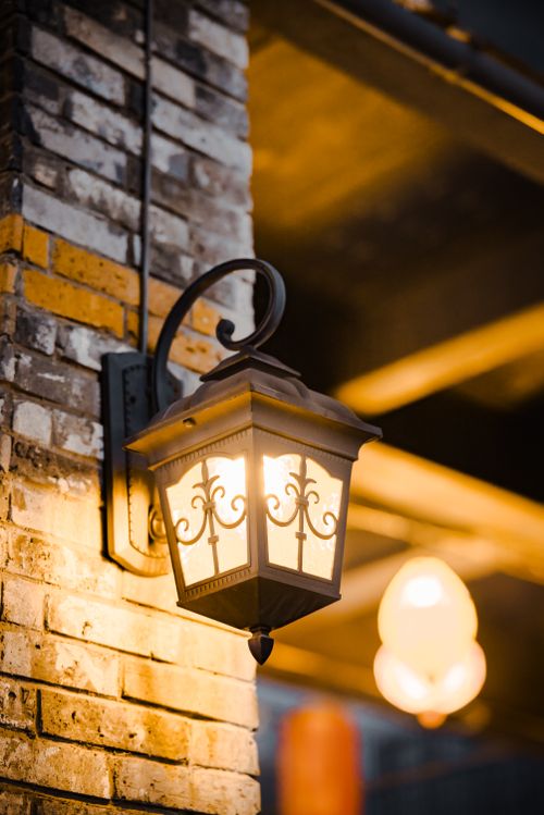 Free Vintage lantern illuminating a rustic brick wall, creating a warm ambiance in a cozy outdoor setting. Stock Photo