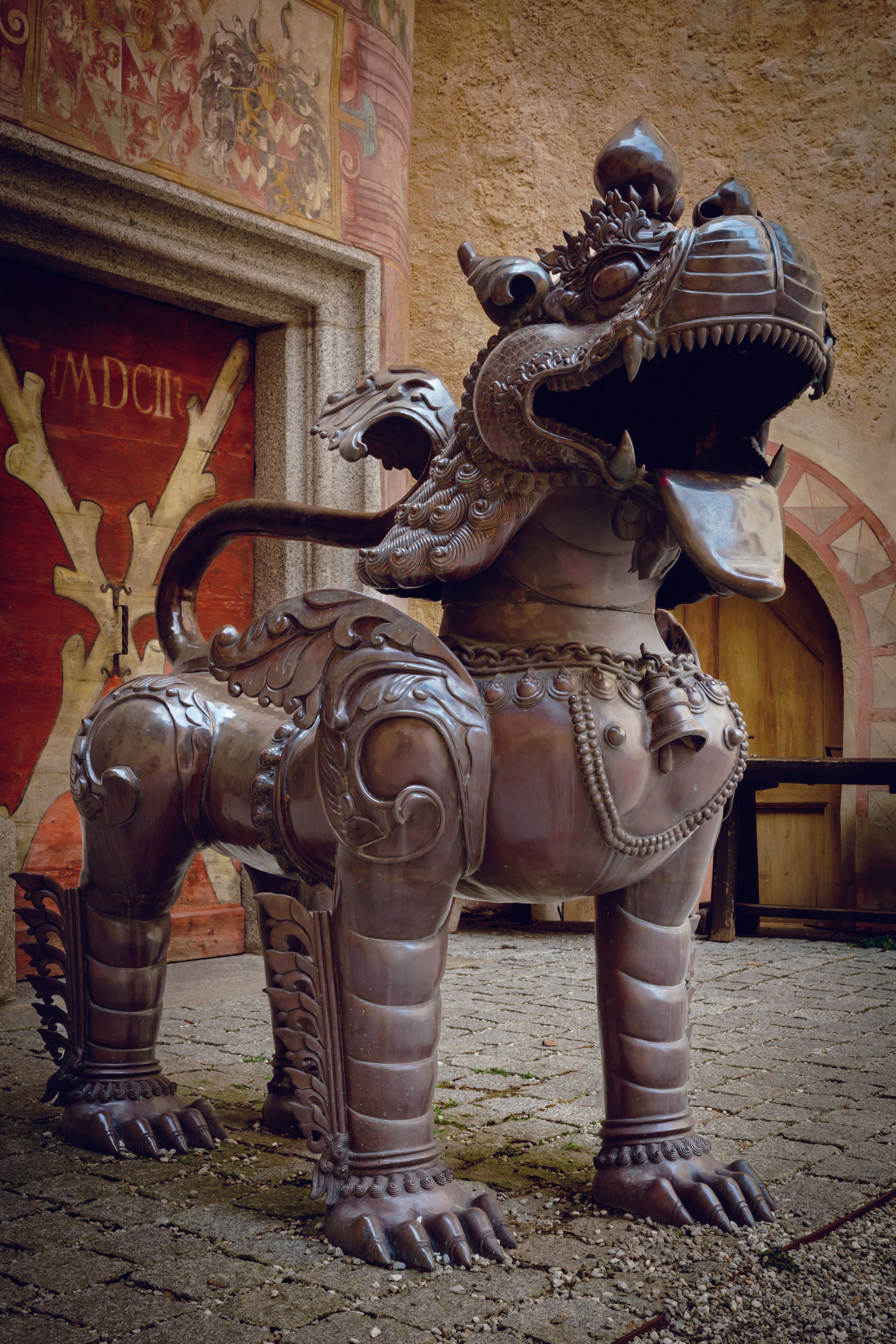 Intricately designed metal dragon statue in a historical courtyard setting. Detailed craftsmanship visible.