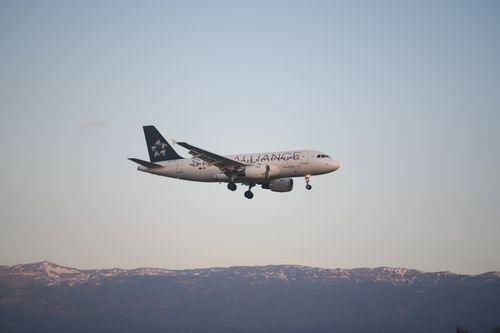 Free Airbus A320 aircraft descending over Geneva with a picturesque mountain backdrop at sunrise. Stock Photo