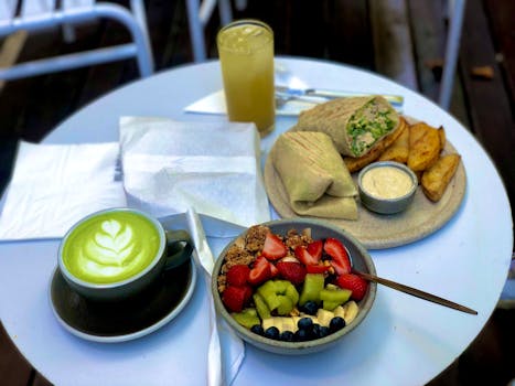Tasty café brunch featuring latte art, fresh fruit bowl, wrap, and fries.