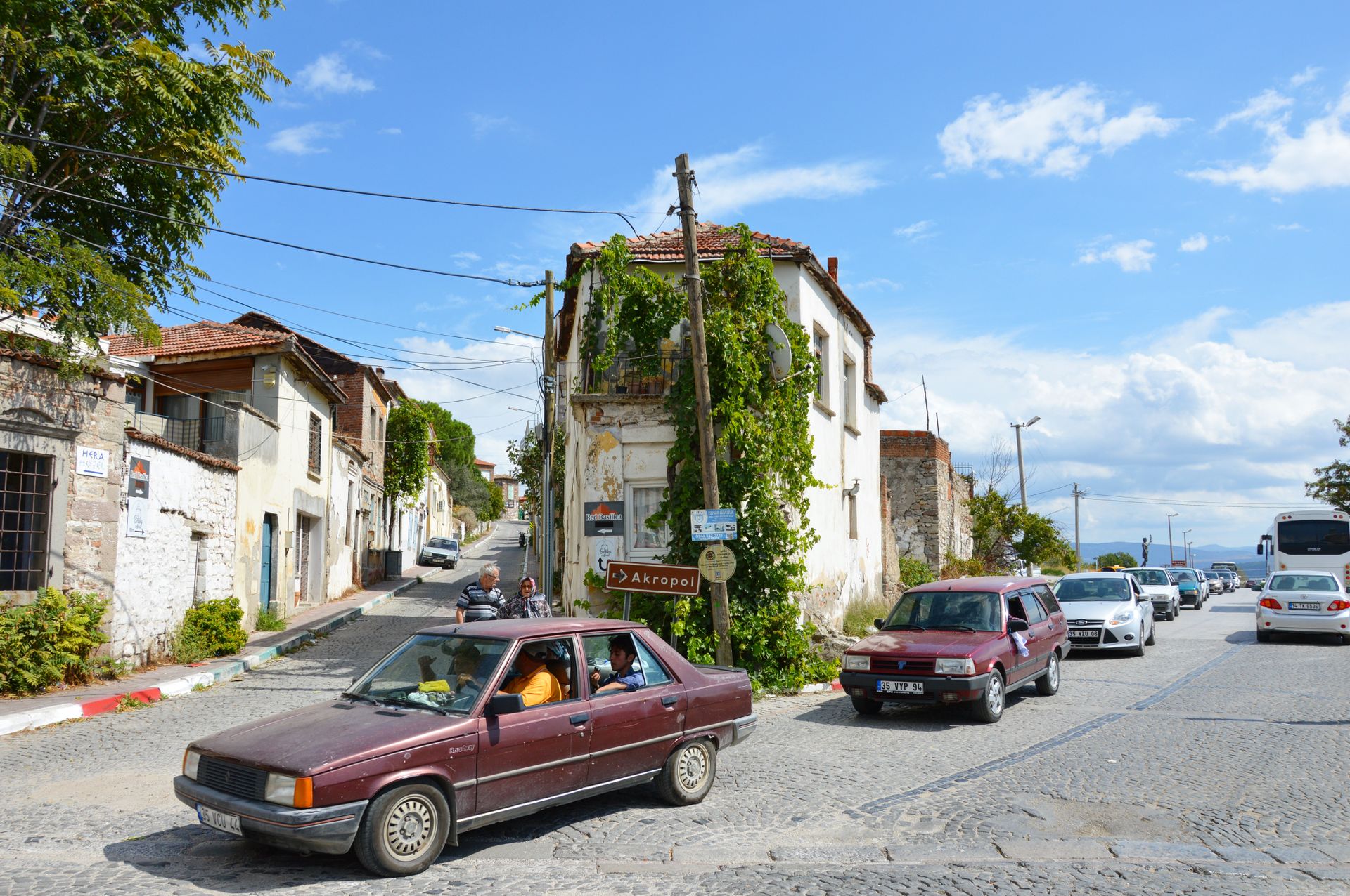 A vibrant street view of a Greek town with vintage cars and historical architecture, showcasing daily life.