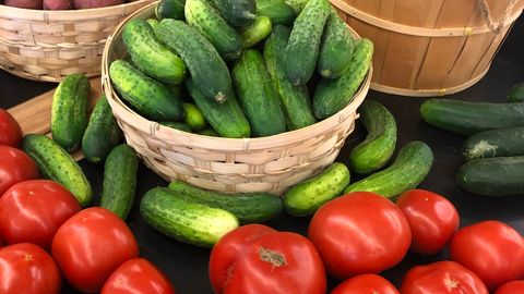 Colorful assortment of fresh vegetables including tomatoes, cucumbers, and sweet potatoes at a market.